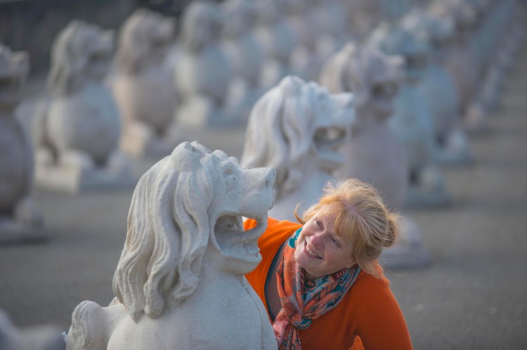 A woman (Gillian Taylor) wearing a bright orange cardigan. She is looking up at a concrete lion sculpture.