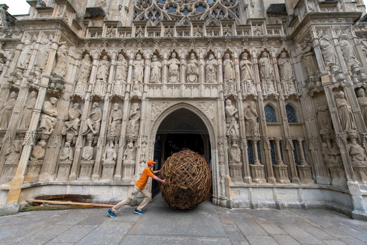A man rolling a huge woven willow ball into the doors of Exeter Cathedral